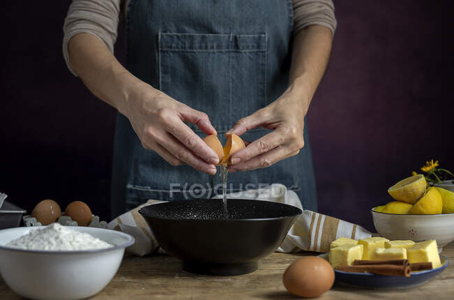 Unrecognizable femmina rompere uovo di pollo fresco in ciotola durante la cottura pasticceria in un tavolo di legno con ingredienti freschi — Foto stock