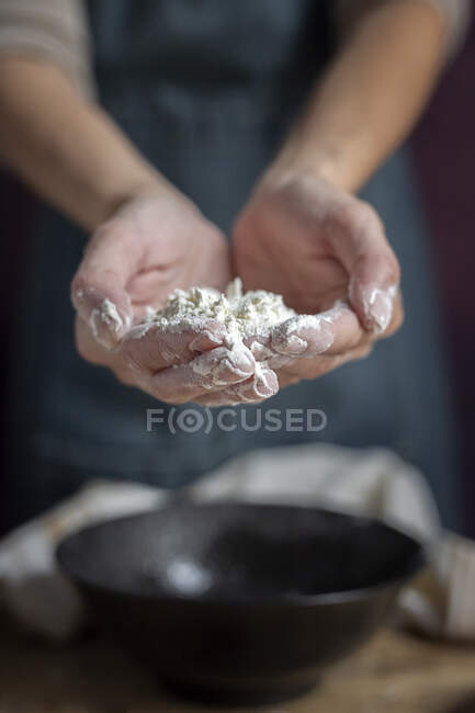 Cropped unrecognizable woman showing hands full of flour near black bowl while preparing pastry at home — Stock Photo
