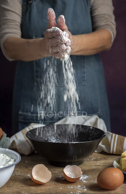 Cropped unrecognizable female spilling wheat flour into bowl near egg egg shells while preparing pastry at home — Stock Photo