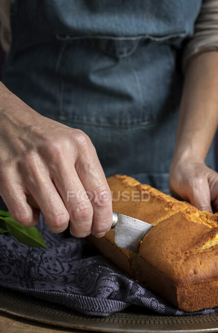 Cortado manos de mujer irreconocibles cortando por la mitad con un cuchillo un pastel de limón casero - foto de stock
