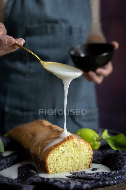 Зверху обрізані невпізнавані жінки руки наливають білу солодку глазур на домашній лимонний торт — стокове фото