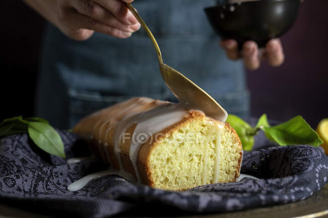 Обрізані невпізнавані руки жінки наливають білу солодку глазур на домашній лимонний торт — стокове фото