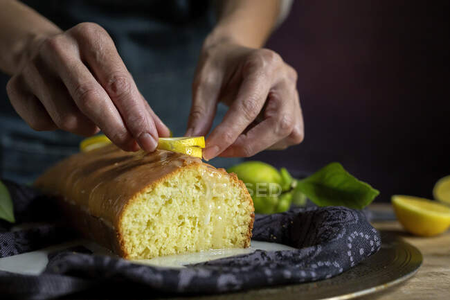 Обрізані невпізнавані руки жінки готують домашній смачний лимонний торт, покритий глазур'ю та лимонними скибочками — стокове фото