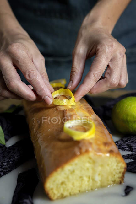 Зверху обрізані невпізнавані руки жінки готують домашній смачний лимонний торт, покритий глазур'ю та лимонними скибочками — стокове фото