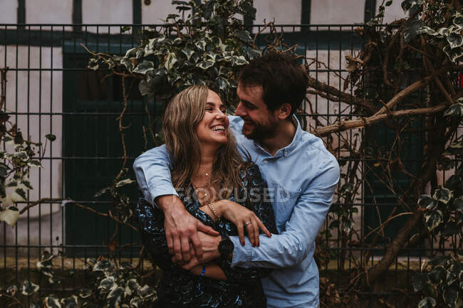 Zufriedene junge Männer und Frauen umarmen und küssen sich, während sie am Metallzaun auf der Stadtstraße stehen und gemeinsam den Sommertag genießen — Stockfoto