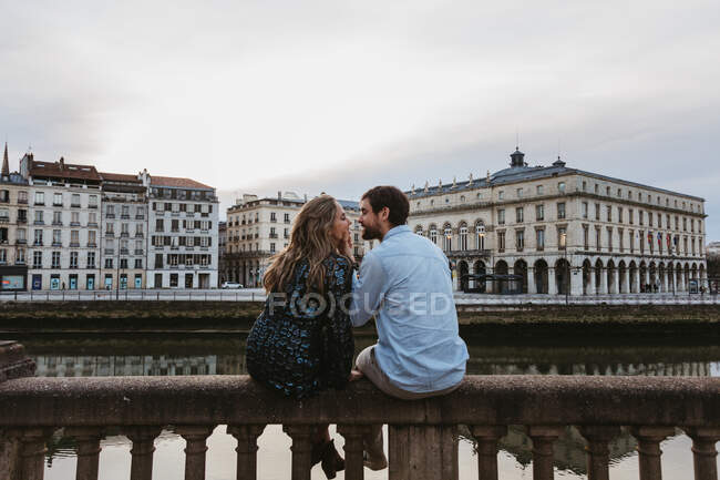 Back view of happy couple sitting embracing each other on old stone fence spending summer evening together in Bayonne — Stock Photo