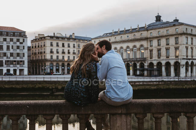 Back view of happy couple sitting kissing each other on old stone fence spending summer evening together in Bayonne — Stock Photo