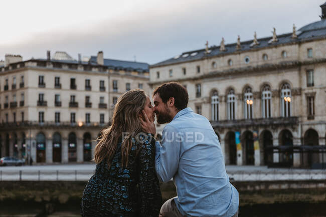 Vista posteriore della coppia felice seduta a baciarsi sul vecchio recinto di pietra trascorrere la serata estiva insieme a Bayonne — Foto stock
