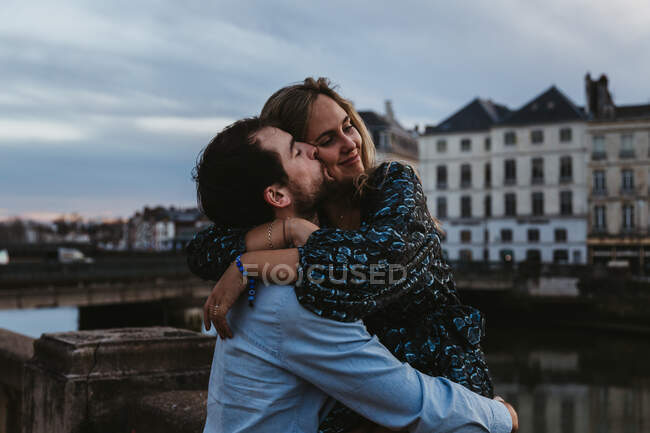 Joyeux jeune femme assise sur une vieille clôture en pierre et embrassant son affectueux petit ami tout en passant la soirée d'été ensemble à Bayonne — Photo de stock