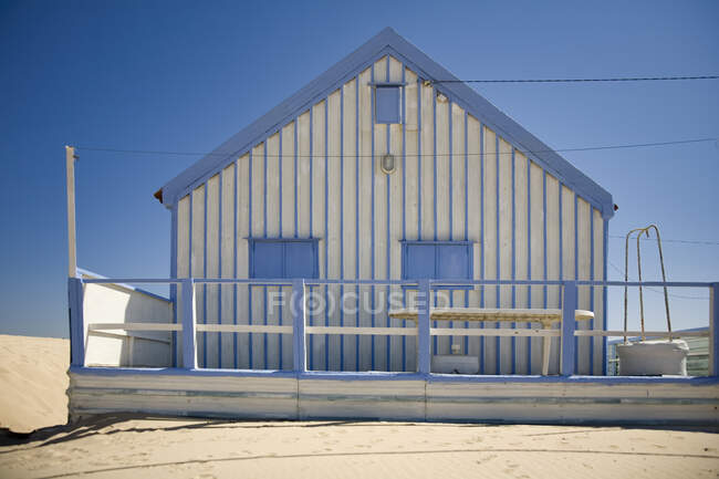 Small white and blue strips country house with white fence located at seaside against cloudless blue sky in sunny day — Stock Photo