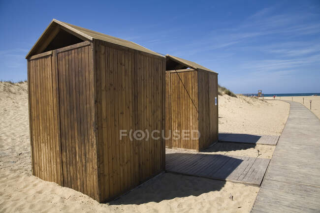 Small plank wooden booths and pathway on sandy seashore in sunny day with blue sky in background — Stock Photo