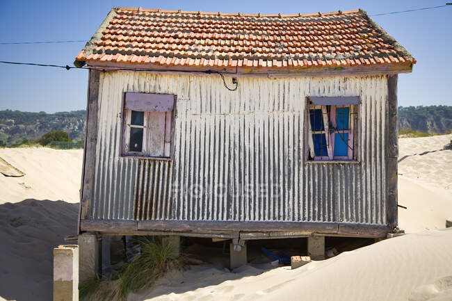 Pequeña casa con paredes de mala calidad situada en la playa de arena con el cielo azul en el fondo en el día soleado - foto de stock