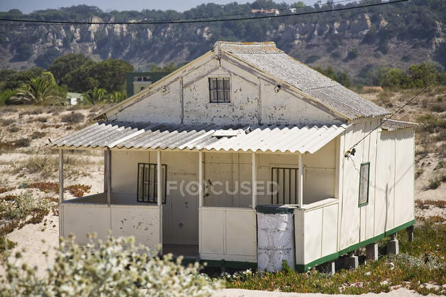 Extérieur d'une petite maison résidentielle aux murs blancs minables construite sur pilotis sur terrain vallonné par temps ensoleillé à la campagne — Photo de stock
