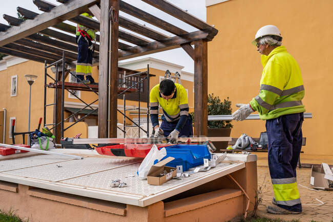 Grupo de técnicos masculinos em uniforme trabalhando com painéis solares alternativos e preparando-se para instalação perto de edifício residencial — Fotografia de Stock
