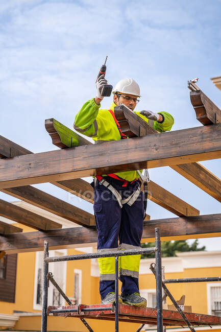 Знизу чоловічий технік у роботі стоїть на риштуванні і готується до установки сонячної панелі на дерев'яну конструкцію — стокове фото
