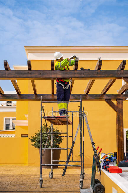 Знизу збоку чоловічий технік у роботі стоїть на риштуванні і готується до установки сонячної панелі на дерев'яну конструкцію — стокове фото