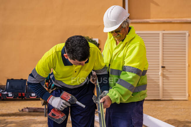 Grupo de técnicos masculinos em uniforme trabalhando com painéis solares alternativos e preparando-se para instalação perto de edifício residencial — Fotografia de Stock