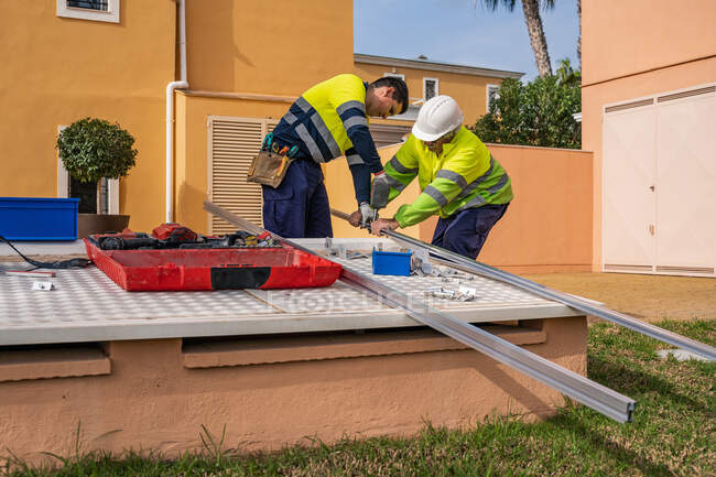 Gruppo di tecnici maschi in uniforme che lavorano con pannelli solari alternativi e si preparano per l'installazione vicino all'edificio residenziale — Foto stock