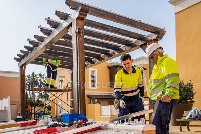 Група техніків-чоловіків в уніформі, що працюють з альтернативними сонячними панелями і готуються до установки біля житлового будинку — стокове фото