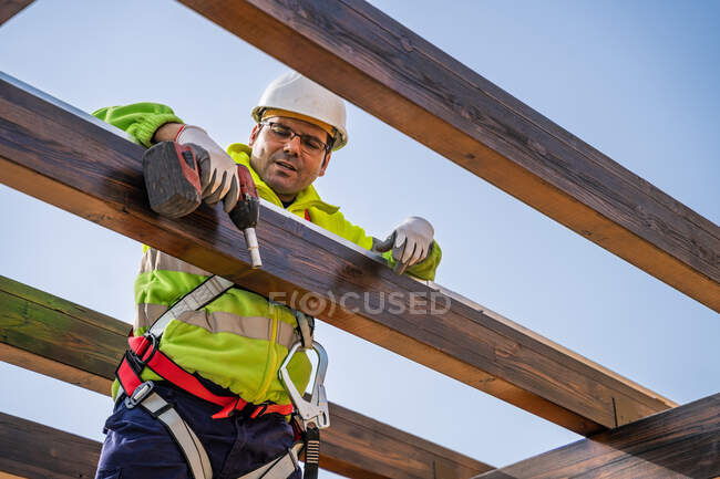 De abaixo do técnico masculino no desgaste do trabalho que está em pé no andaime e se prepara para a instalação do painel solar na construção de madeira — Fotografia de Stock
