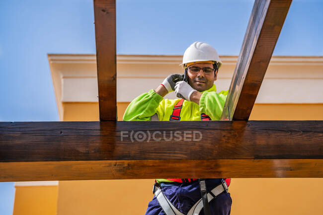 Dal basso di tecnico maschile in usura da lavoro in piedi su impalcatura e preparazione per l'installazione di pannello solare su costruzione in legno — Foto stock