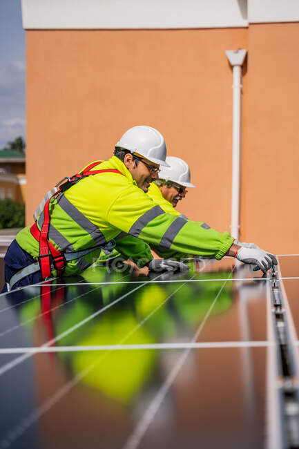 Gruppe von Arbeitern in Uniform und Helmen installiert Photovoltaik-Paneele auf dem Dach einer Holzkonstruktion in der Nähe des Hauses — Stockfoto