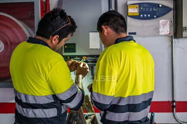 Back view of group of professional male technicians with electric tools repairing and checking equipment while working in building — Stock Photo