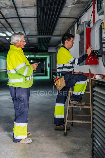 Vista lateral do grupo de técnicos profissionais do sexo masculino com ferramentas elétricas de reparação e verificação de equipamentos durante o trabalho na construção — Fotografia de Stock