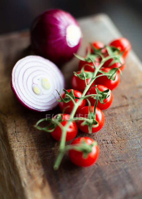 Manojo de tomates maduros frescos cereza y cortar bulbos de cebolla roja colocados en la tabla de cortar de madera - foto de stock