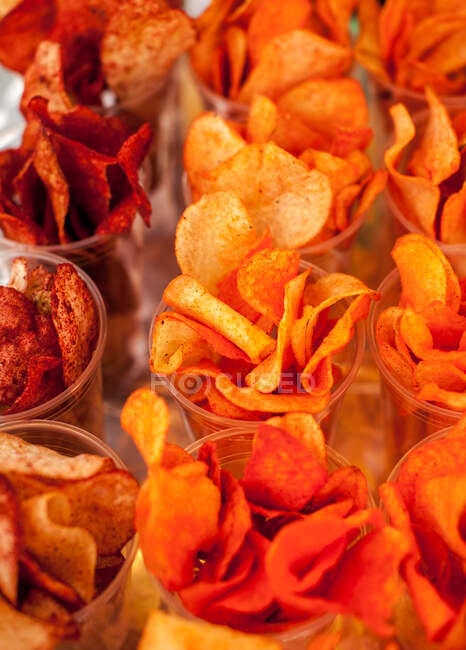 Von oben Lebensmittel Hintergrund mit verschiedenen leckeren pikanten Chips knusprig serviert in kleinen Plastikbechern — Stockfoto