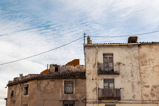 Angle bas de vieilles maisons en pierre ruinée avec murs et balcons minables situés dans le quartier de la ville contre un ciel nuageux — Photo de stock