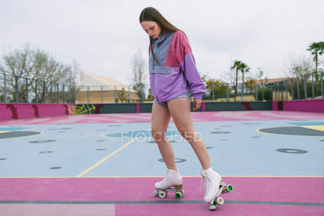Низький кут молодої жінки в модному спортивному одязі з чотирма роликовими ковзанами тренування на барвистому ігровому майданчику навесні — стокове фото