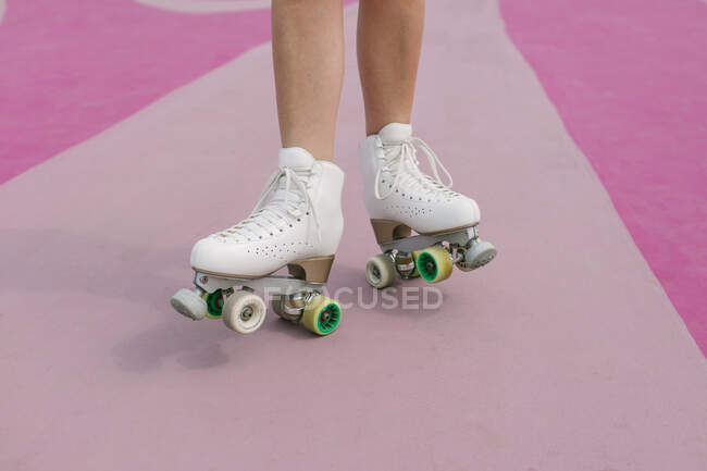 De haut de la récolte femelle anonyme sur des patins à roulettes blancs vintage debout sur un terrain de sport rose — Photo de stock