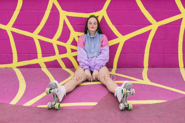 Adolescente alla moda con pattini a rotelle seduto vicino al muro rosa — Foto stock