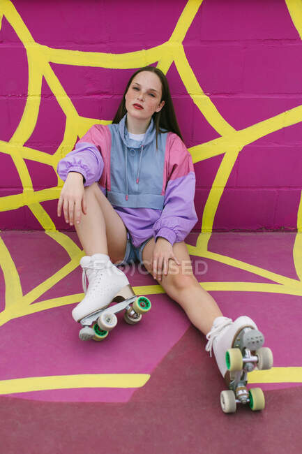Adolescente alla moda con pattini a rotelle seduto vicino al muro rosa — Foto stock