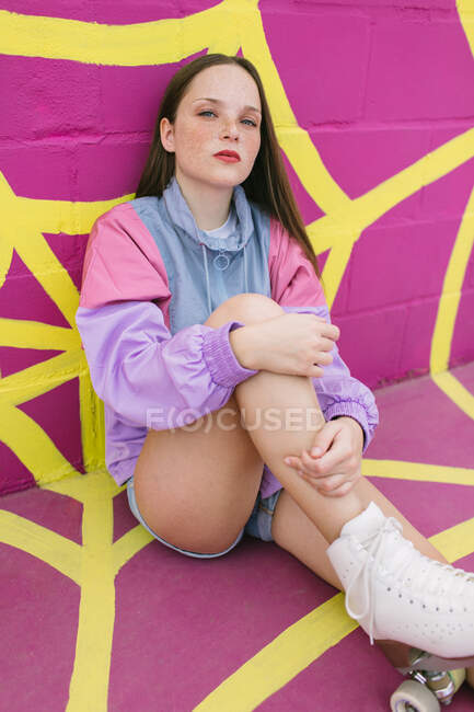 Adolescent branché avec patins à roulettes assis près du mur rose — Photo de stock