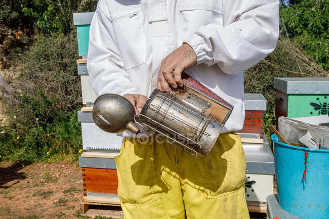 Closeup of crop anonymous male beekeeper making fire on bee smoker while working on apiary — Stock Photo