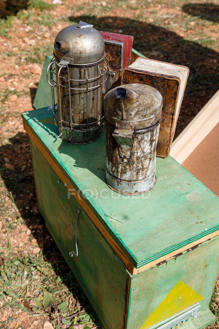 From above of old metal bee smokers placed on green wooden beehive box in apiary in sunny summer day — Stock Photo