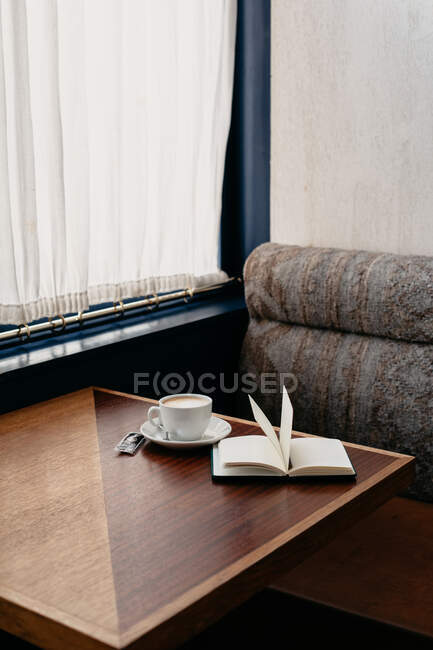Primer plano de una taza de café y un libro sobre una mesa - foto de stock