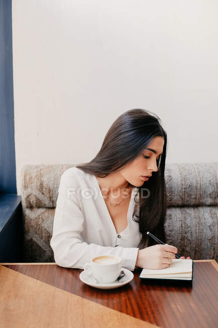 Brünette Frau schreibt in einem Notizbuch in einer Bar — Stockfoto