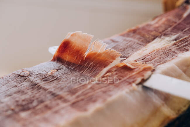 From above view of knife cutting thin slice of ham with tallow lines — Stock Photo