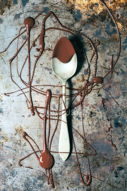 From above top view spoon with chocolate spilled over rustic metal surface background — Stock Photo