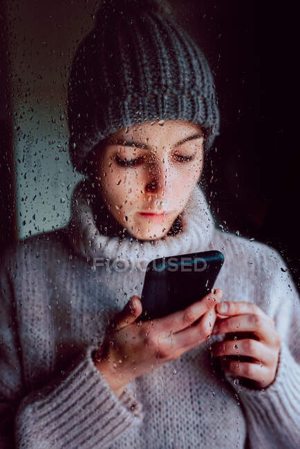 Mujer joven con smartphone de pie cerca de la ventana - foto de stock