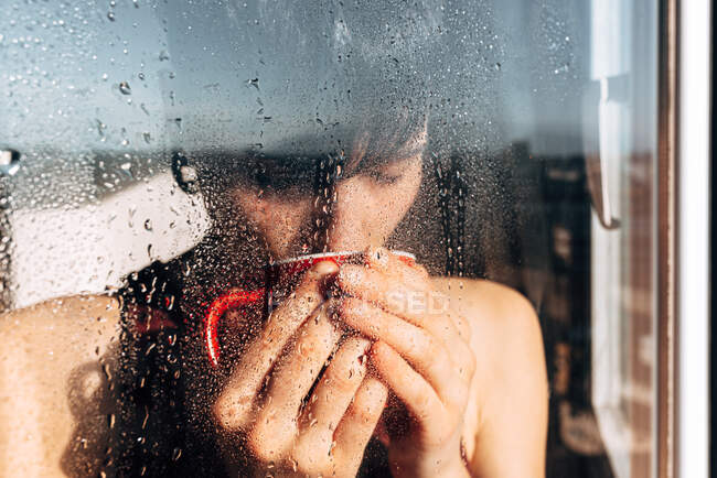 Задумчивая женщина пьет кофе у окна — стоковое фото
