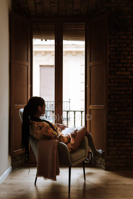 Mulher étnica com livro descansando em casa — Fotografia de Stock
