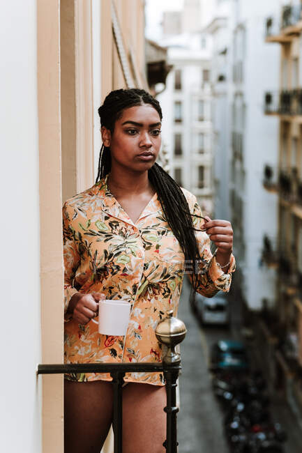 Молода жінка з чашкою кави стоїть на балконі — стокове фото