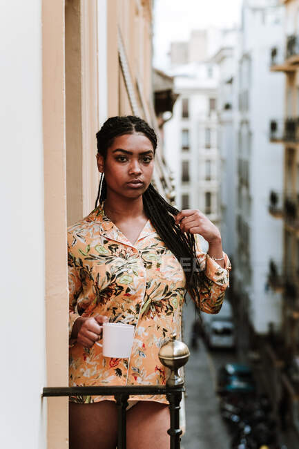 Junge Frau mit Tasse Kaffee steht auf Balkon — Stockfoto