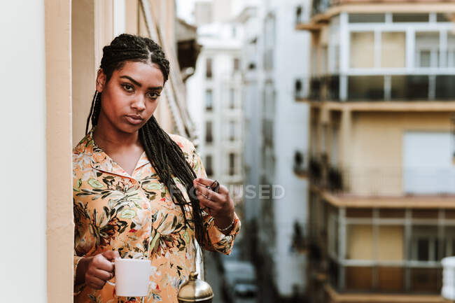 Young woman with cup of coffee standing on balcony — Stock Photo