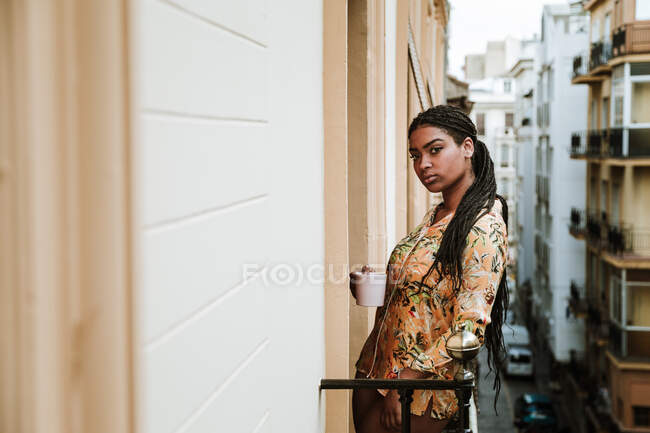 Giovane donna con tazza di caffè in piedi sul balcone — Foto stock