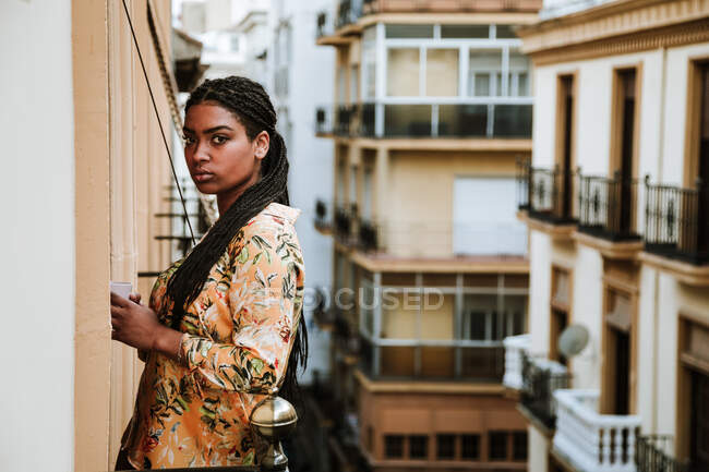 Young woman with cup of coffee standing on balcony — Stock Photo